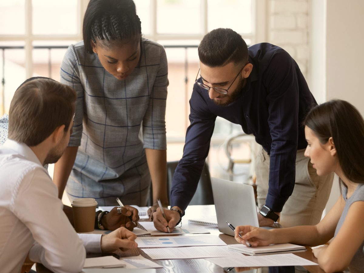 People working around a table. One man and one woman are standing and taking notes.